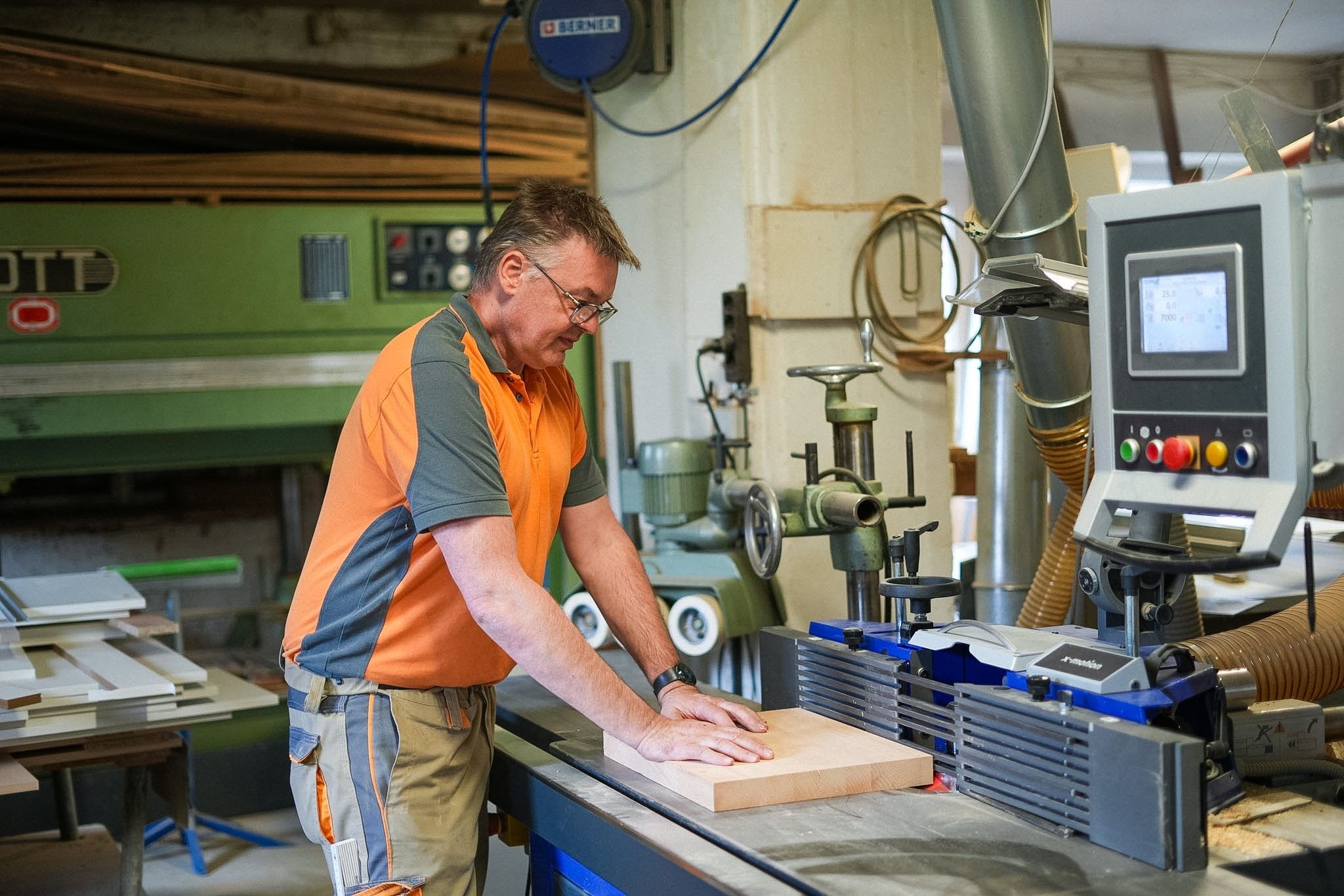 Jörg Häfner führt ein Buchenbrett über den Tisch einer Maschine mit digitaler Steuerung; im Hintergrund weitere Werkstattmaschinen und eine Absauganlage.