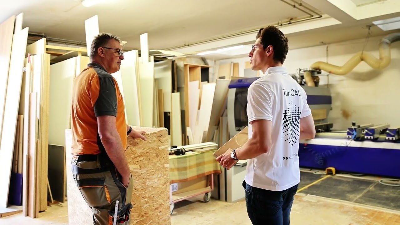Jörg Häfner im Gespräch mit einem Mitarbeiter von TRUN CAD in der Werkstatt, zwischen aufgestellten Plattenzuschnitten.